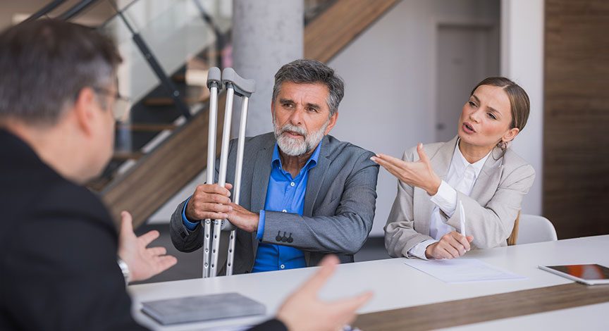 injured-worker-on-crutches-meeting-with-two-people-over-paperwork
