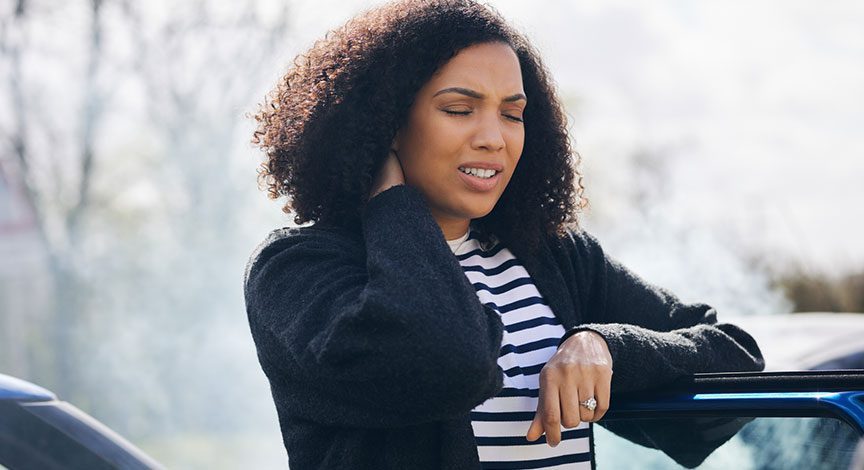 woman-holding-her-neck-while-standing-outside-car